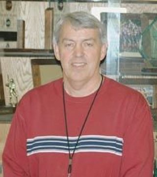 LHS physical education teacher and fastpitch softball coach Steve Barker poses in front of the softball trophy case.