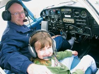 James Nice helps seven-year-old Arlington resident Payton Brown strap herself into the cockpit of his Piper Cherokee and perform the needed preflight checks before they take off together.