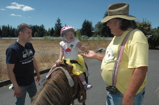 Arlington's Nick Ernst looks on as his daughter Lacey high-fives 'Buckaroo Bob' during a pony ride at the July 27 business fair to help raise funds for her heart transplant.
