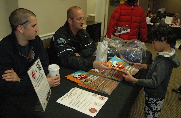 Arlington firefighters Cody Kraski and Wayne Mitchell pass out educational goodies to Gabe Seagraves during the Stillaguamish Athletic Club’s Health and Fitness Fair on Nov. 4.