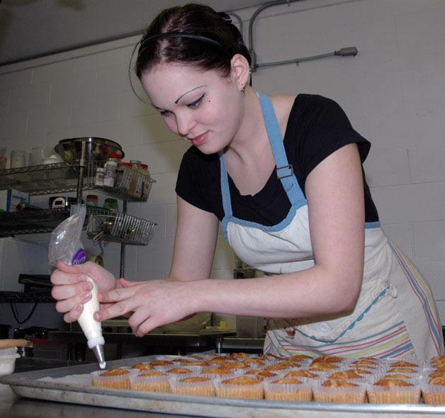 Kat Nixon puts the final touches on a tray of cupcakes at Petite Sweet.