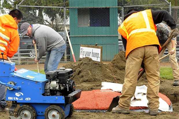 Workers dig a pit so they can turn that mound upside down.