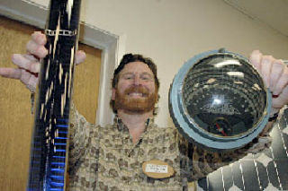 Chris Herman of Winter Sun Design holds up in his right hand a solar vacuum tube for a baby solar hot water maker