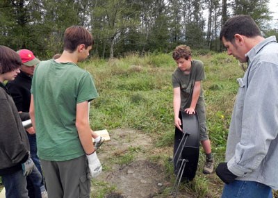 Kennedy Englert’s volunteers look on as he explains how to install the firepits at the Country Charm Park and Recreation Area in Arlington.