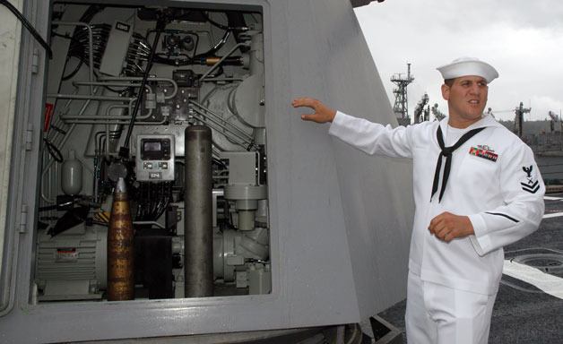 Petty Officer 2nd Class Justin Clark explains the inner workings of the computer-guided 5-inch 62-caliber gun near the forecastle of the USS Shoup on June 30.