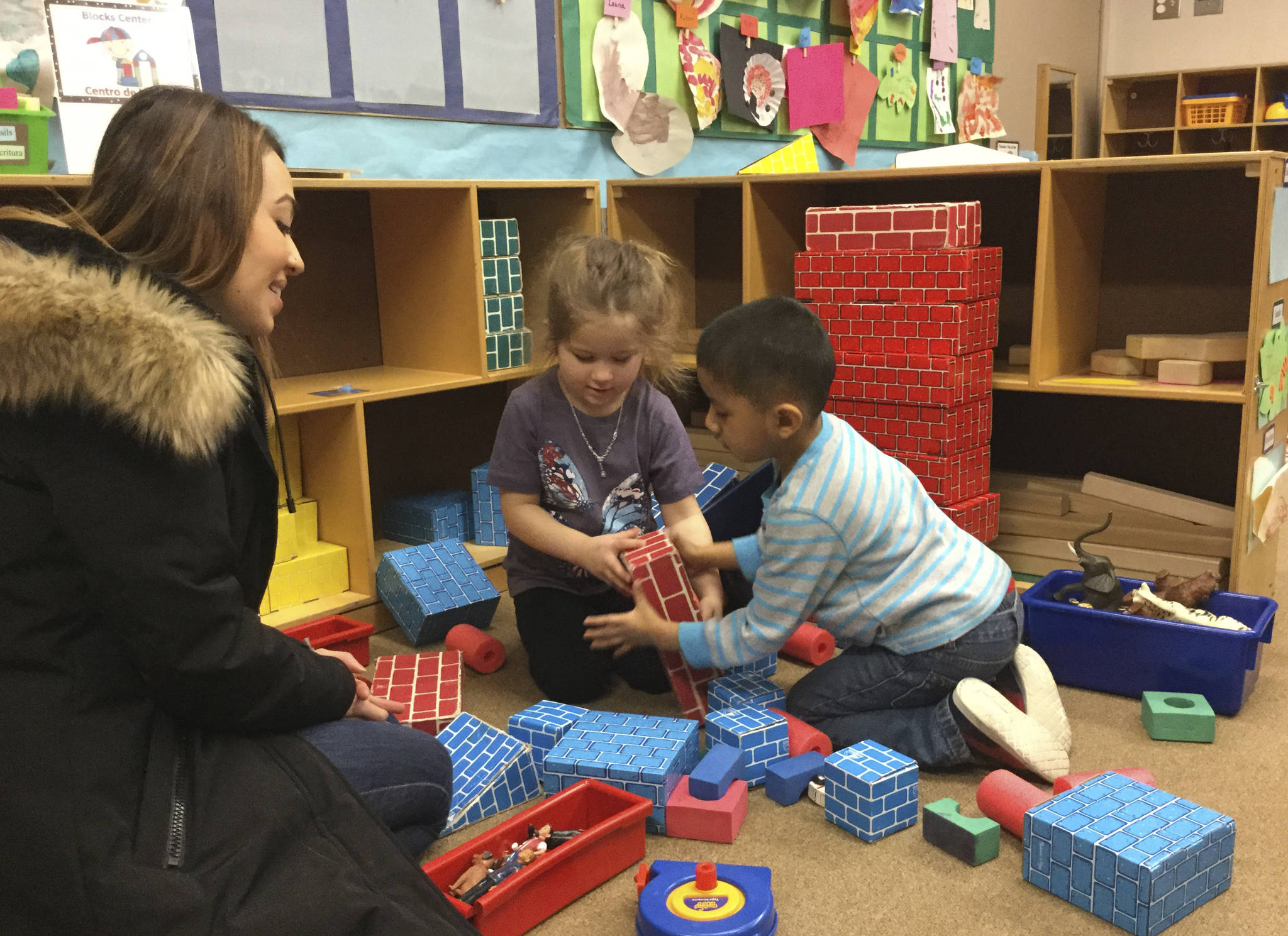 Arlington ECEAP teacher Tina Stivala-Bliss looks on as 4-year-old preschoolers Joonbug Blunt and Jonathan Solano work together to build a block tower.