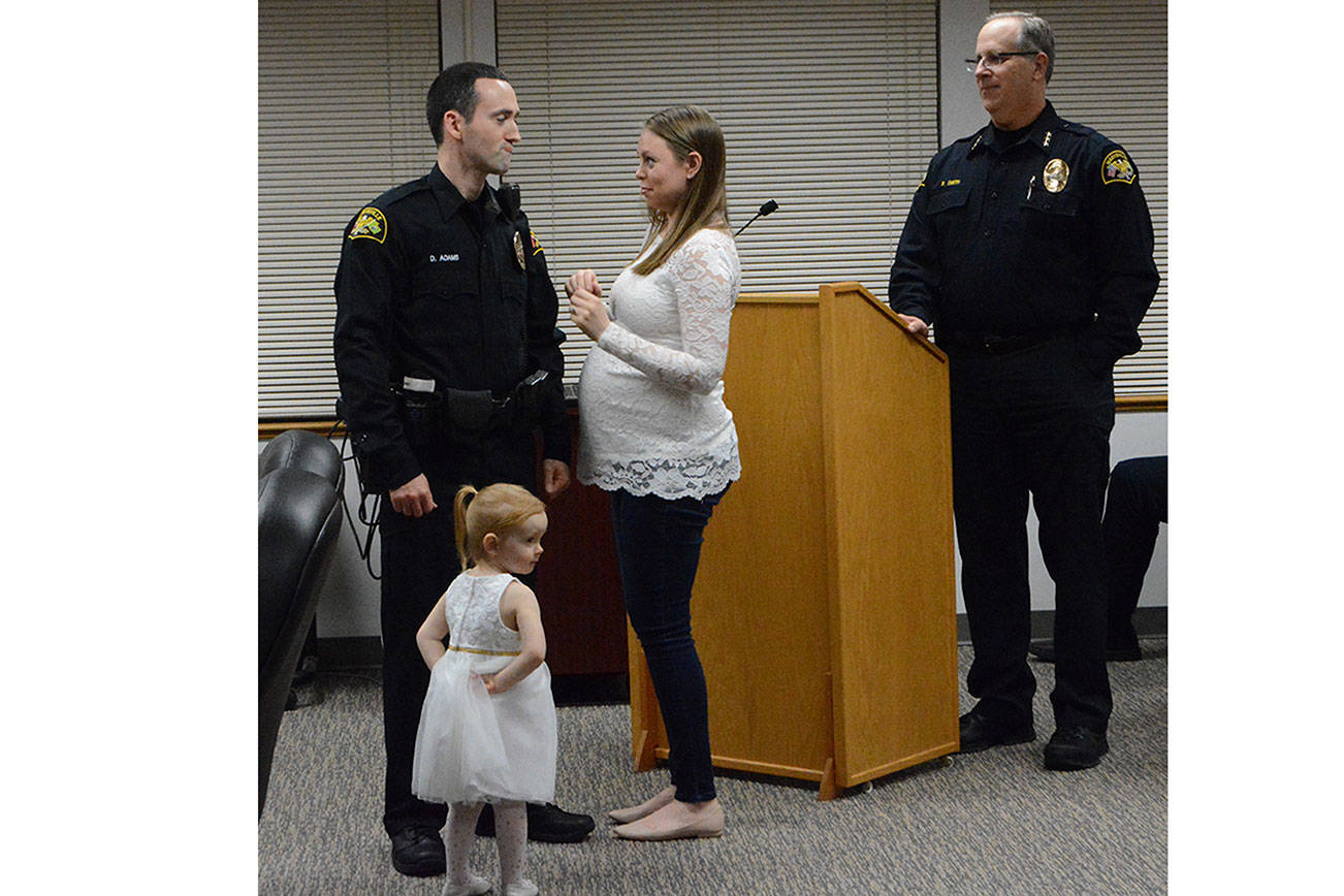 New Marysville police officer Dave Adams exchanges a glance with his wife, Emily, after she pinned his badge on him at Monday’s City Council meeting. Police Chief Rick Smith watches along with their daughter, Olivia, 2. The Adams family is expecting a son to be born in April. (Steve Powell/Staff Photo)
