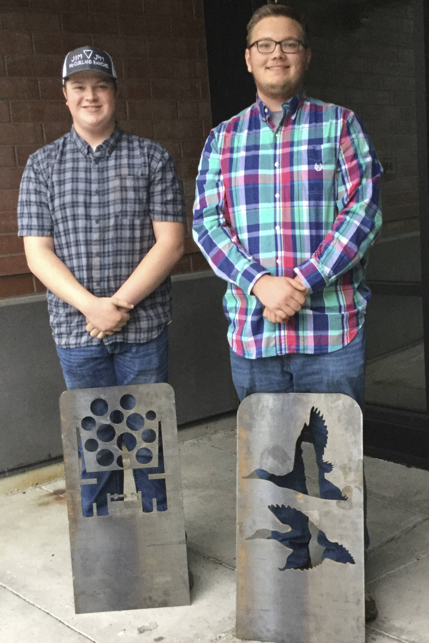 From left, Arlington High School welding students Hunter Urionaguena and Ian Seward display the artistic shadow bike racks they designed as part of a school project. The pieces are called “shadow” racks because they cast a shadow on the ground of the image cut into the metal. The racks will be installed downtown in front of various stores.