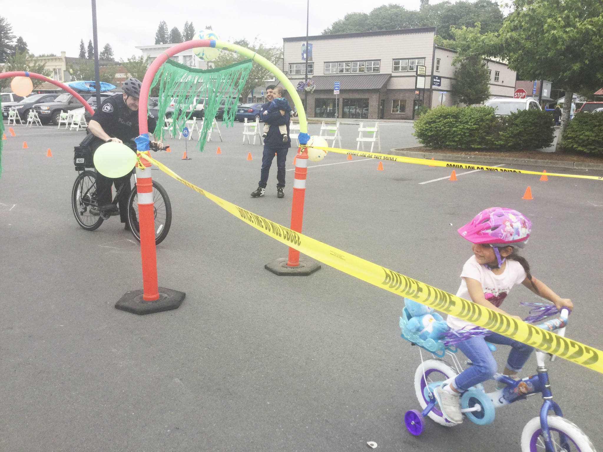 Police Chief Jonathan Ventura helps 4-year-old Delilah Ramos of Arlington navigate an obstacle course at Saturday’s bike rodeo in Legion Park, while father Noe and son Benjamin look on.