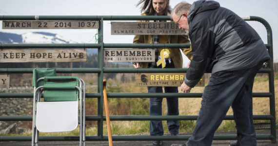 Jennifer Thompson, left, and her father Ron Thompson secure a new remembrance plaque to the Oso slide site gate on Sunday, near Oso. Ron Thompson handcrafts a new plaque for the gate every year. (Olivia Vanni / The Herald)