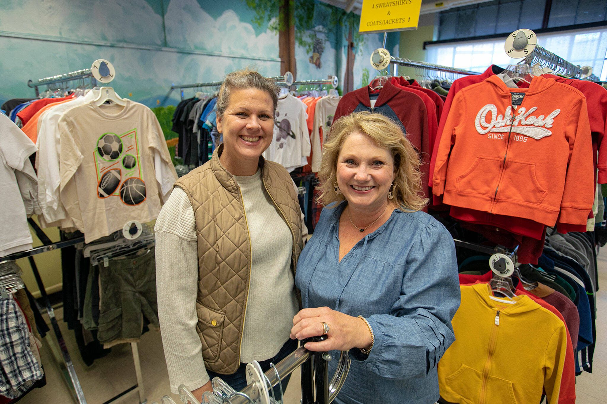 Site Manager LaCrissa Spencer and Director and Cofounder Kimberly Meno stand together among shirts and jackets at Arlington Kids’ Kloset on Nov. 17, in Arlington. (Ryan Berry / The Herald)
