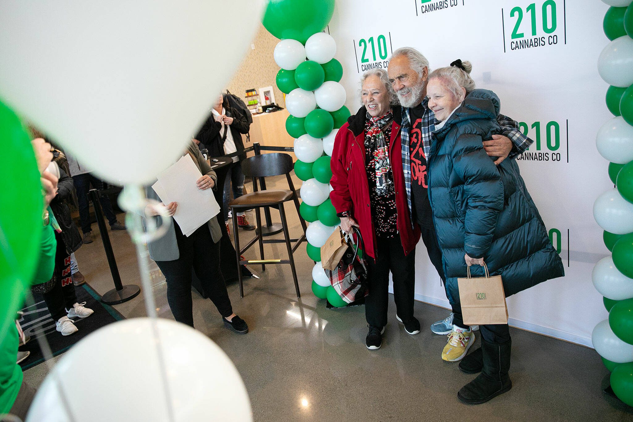 Carla Fisher and Lana Lasley take a photo together with Tommy Chong during 210 Cannabis Co’s grand opening Dec. 10, in Arlington. Fisher and Lasley waited in line solely to get a photo with Chong. (Ryan Berry / The Herald)